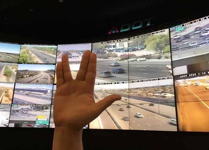 Vulcan hand greeting in front of Traffic Operations Centers wall of traffic monitors.