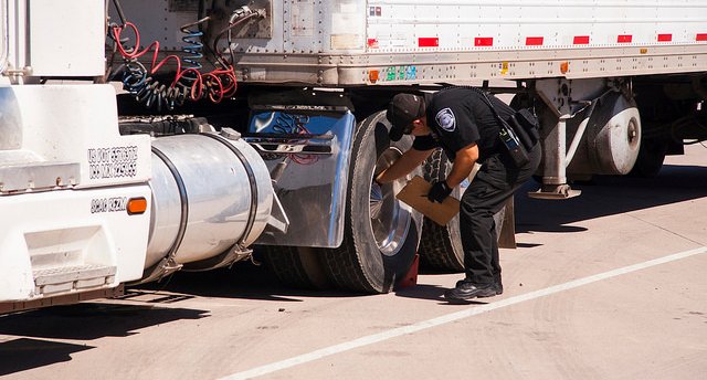 ECD Officer check a tractor trailers tires at an inspection station.