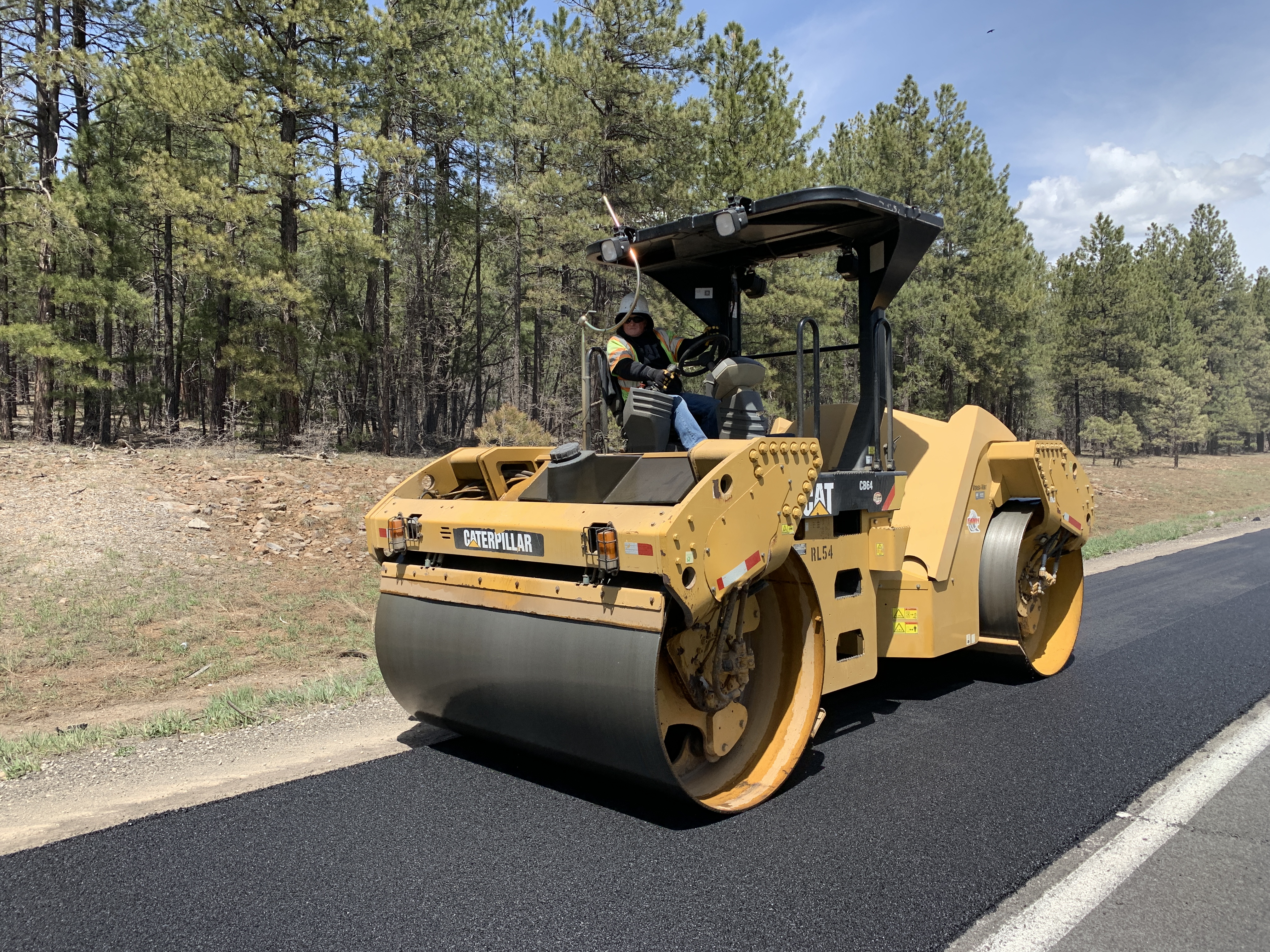 A roller flattens and smooths new asphalt on a highway.
