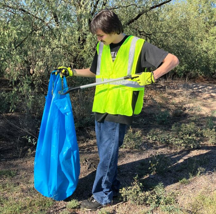 A man in a reflective yellow vest picks up litter along a highway.