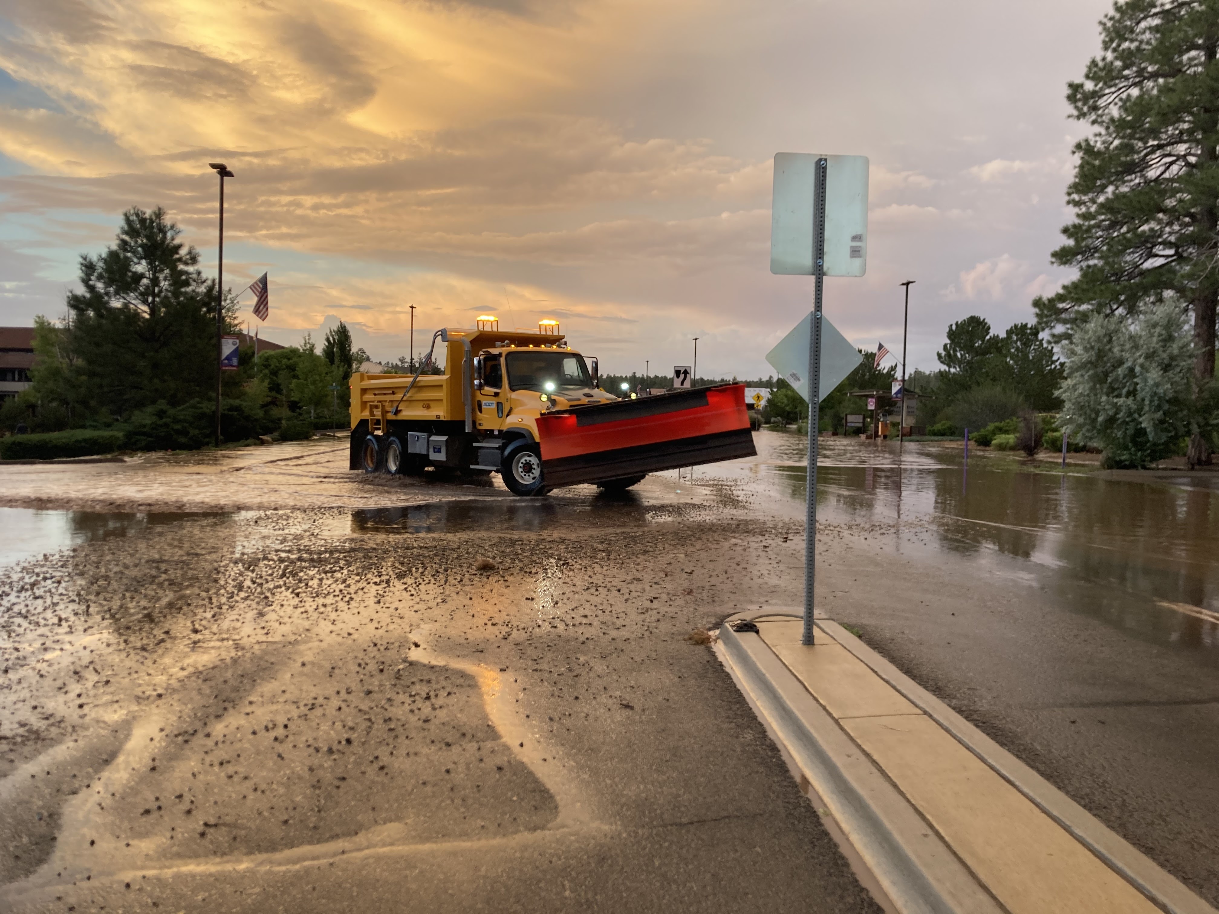A snow plow in a flooded street clears water and debris from the roadway after rainstorm.