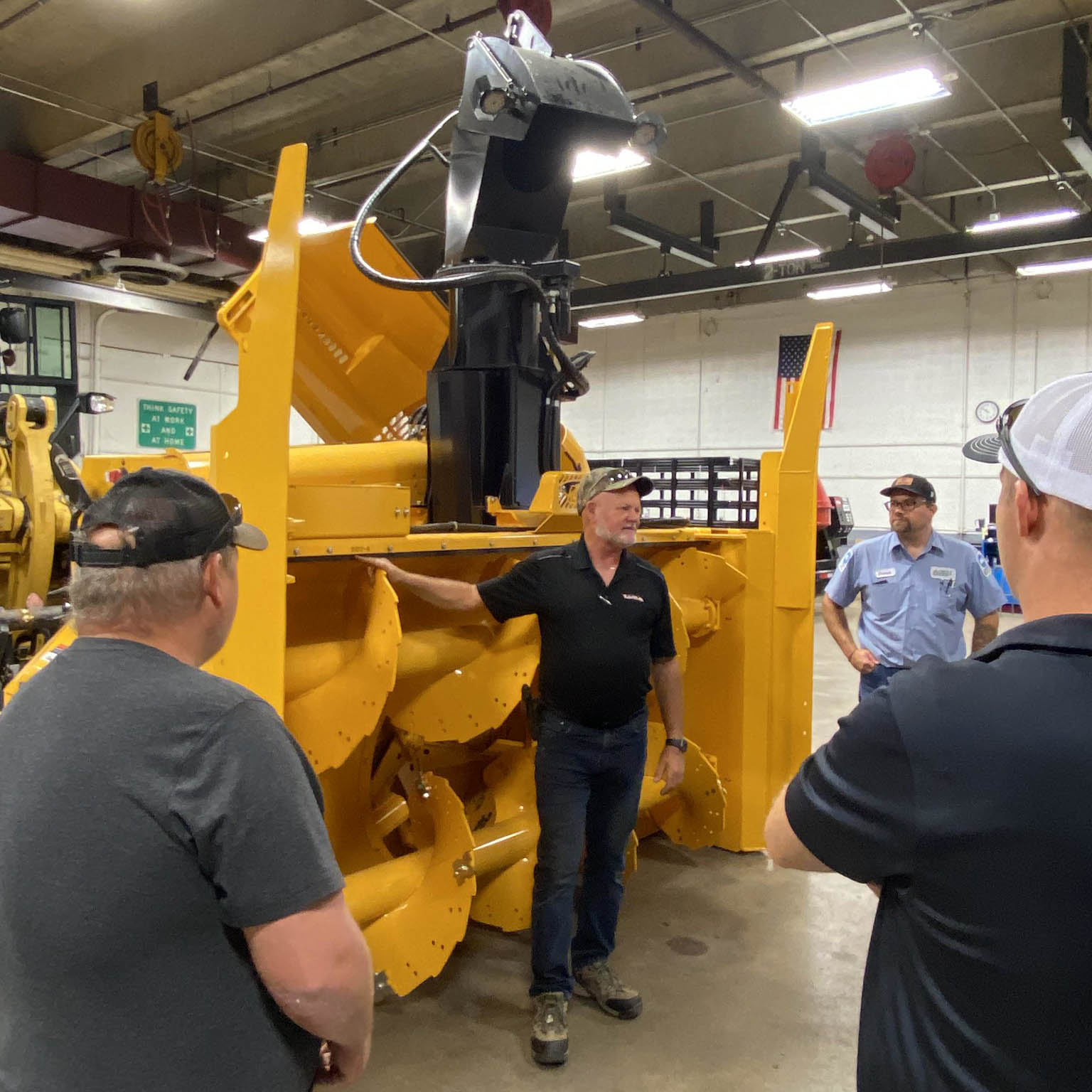 A group of people are gathered around a heavy-duty snowblower and receiving training on how to use the snowblower.