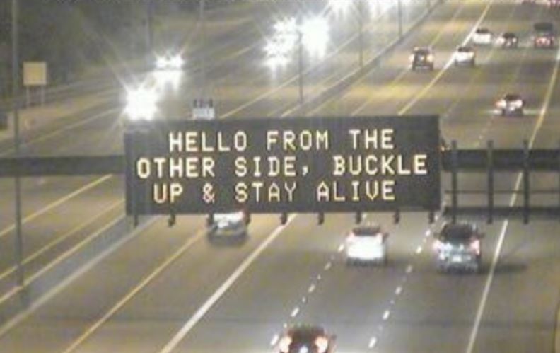 An overhead message board displaying a traffic safety message on a highway.