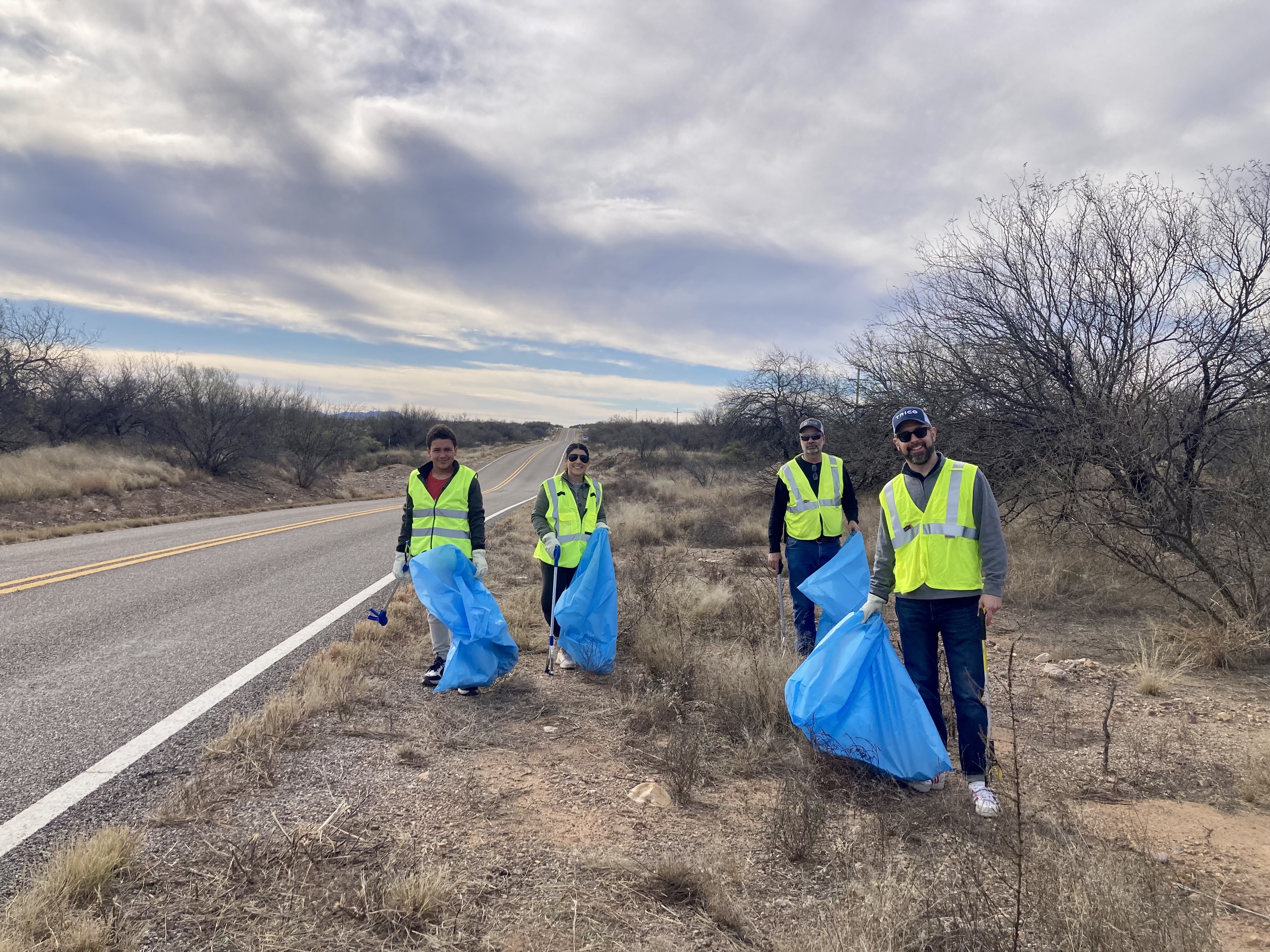 Four volunteers all holding blue trash bags while cleaning up the highway.