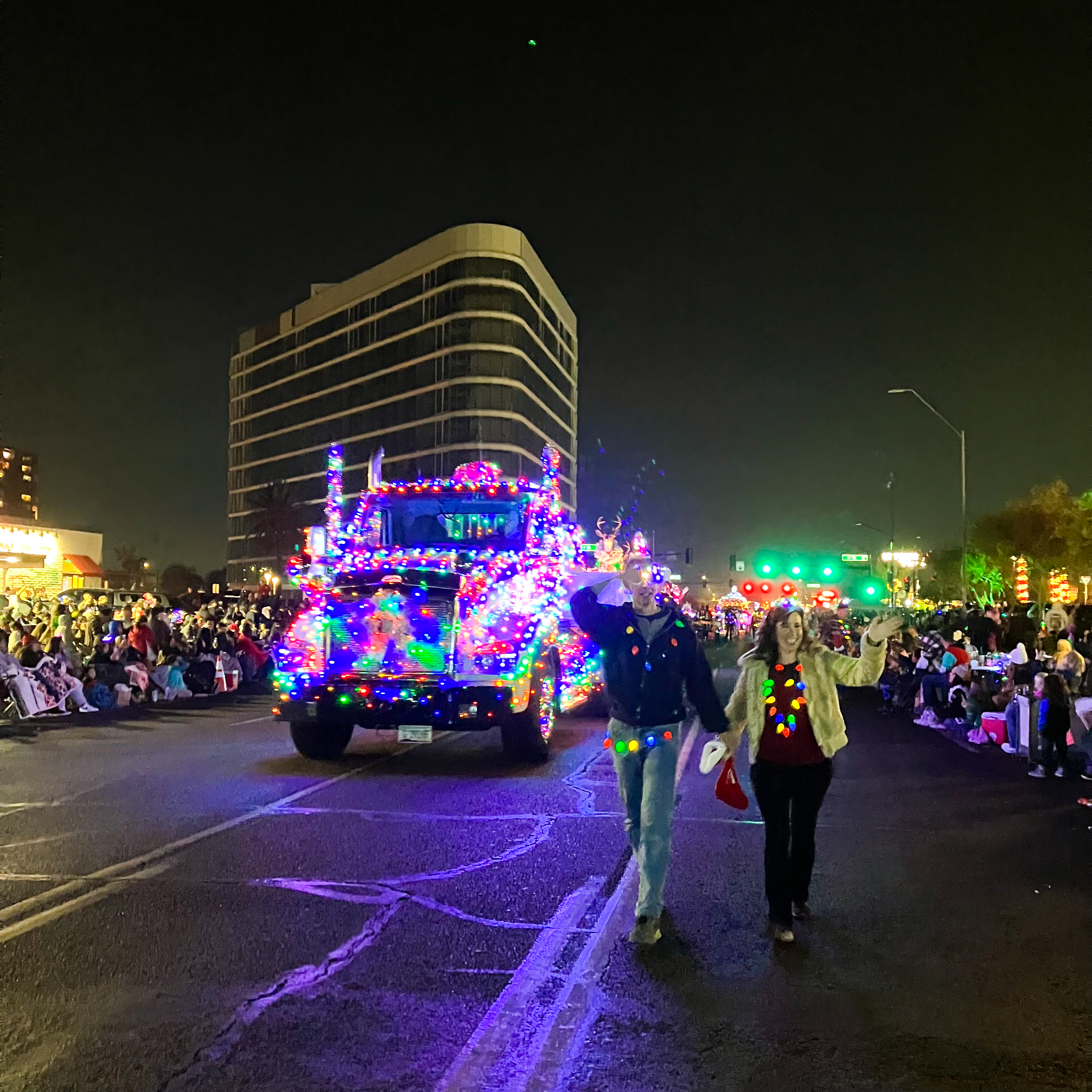 Two ADOT volunteers walking down the street in front of a semi truck decked out in Holiday lights for the Electric Light Parade.