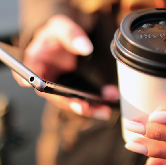 A cell phone is held in a person's hand and a coffee cup is in the other hand.