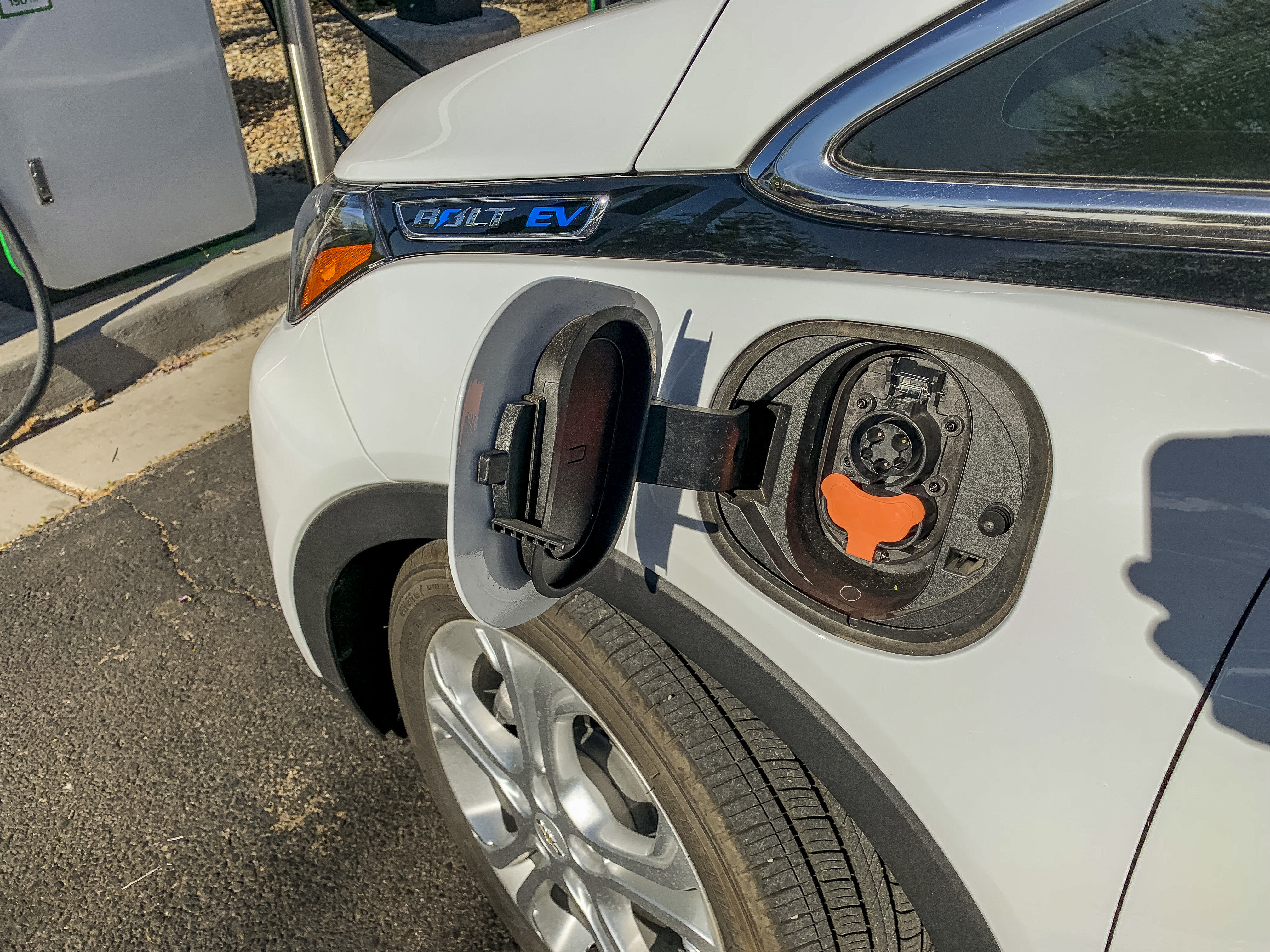 An electric vehicle with an open charge port is parked at a charging station.