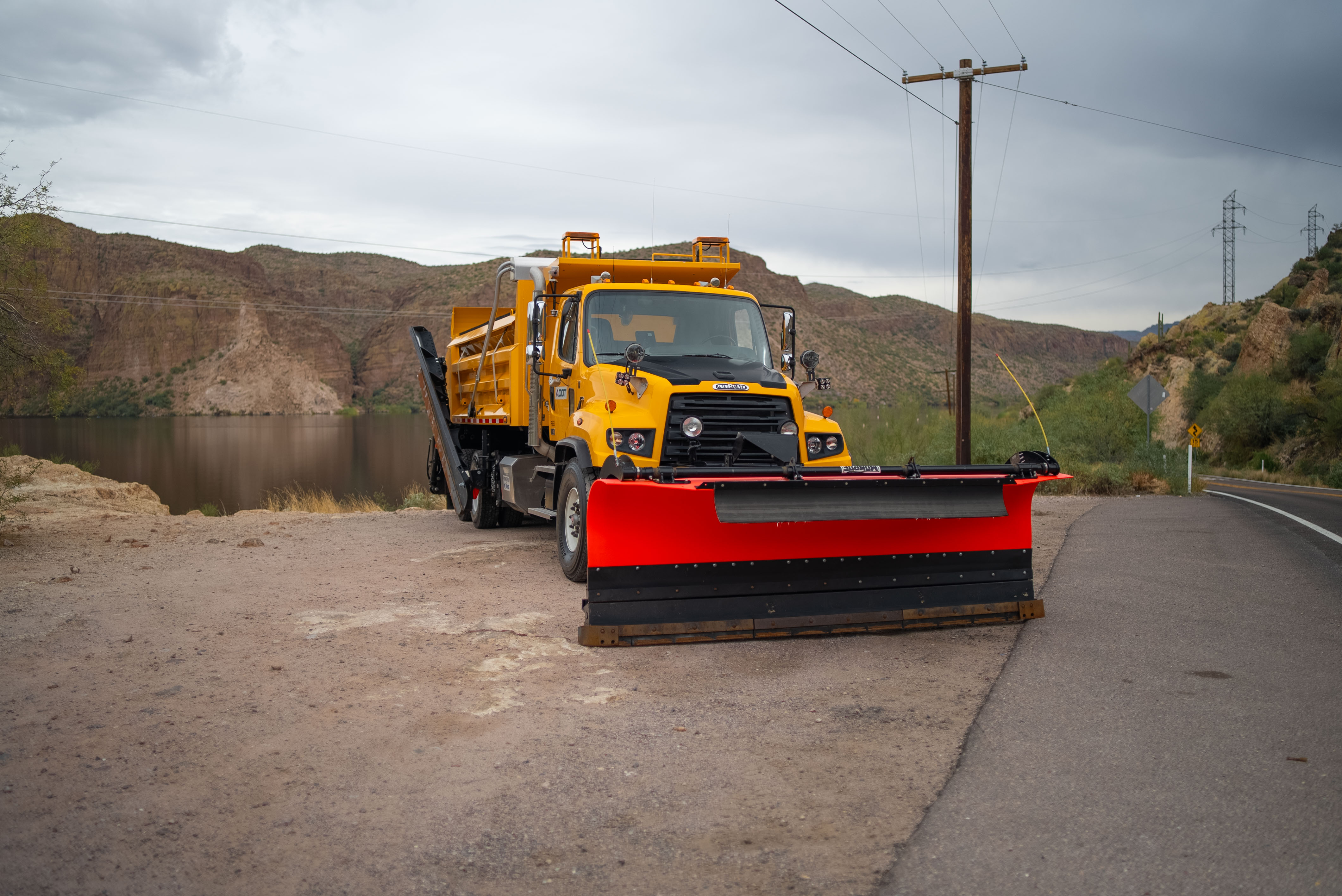 A snowplow parked in front of a lake and mountains.