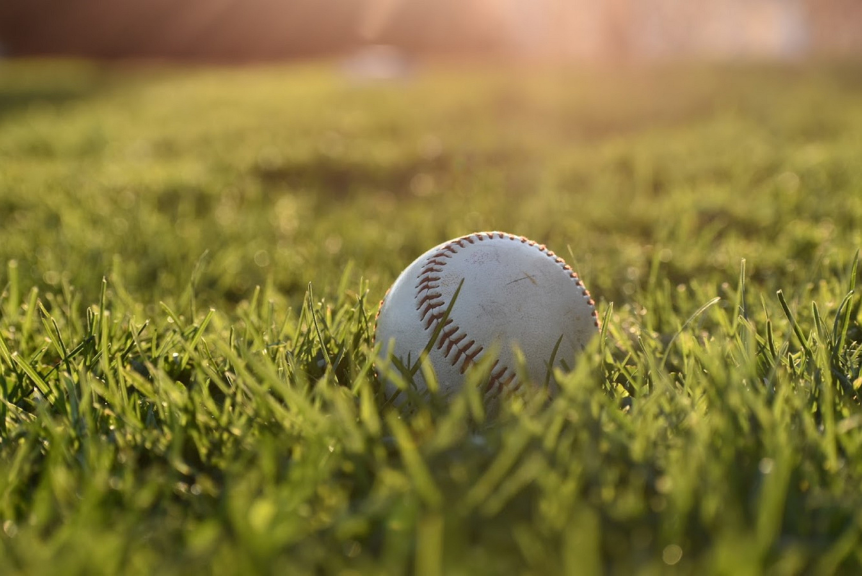 A baseball lies on grass as sun shines in the background.