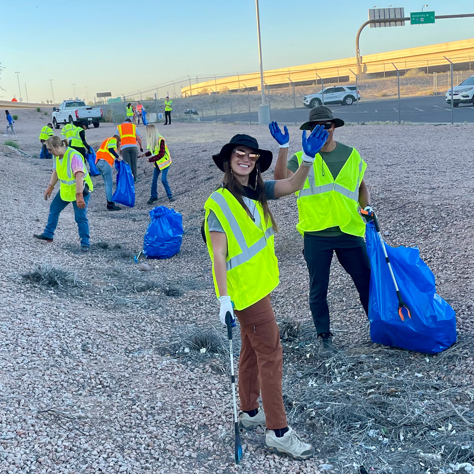 A group of volunteers pick up litter near a highway.