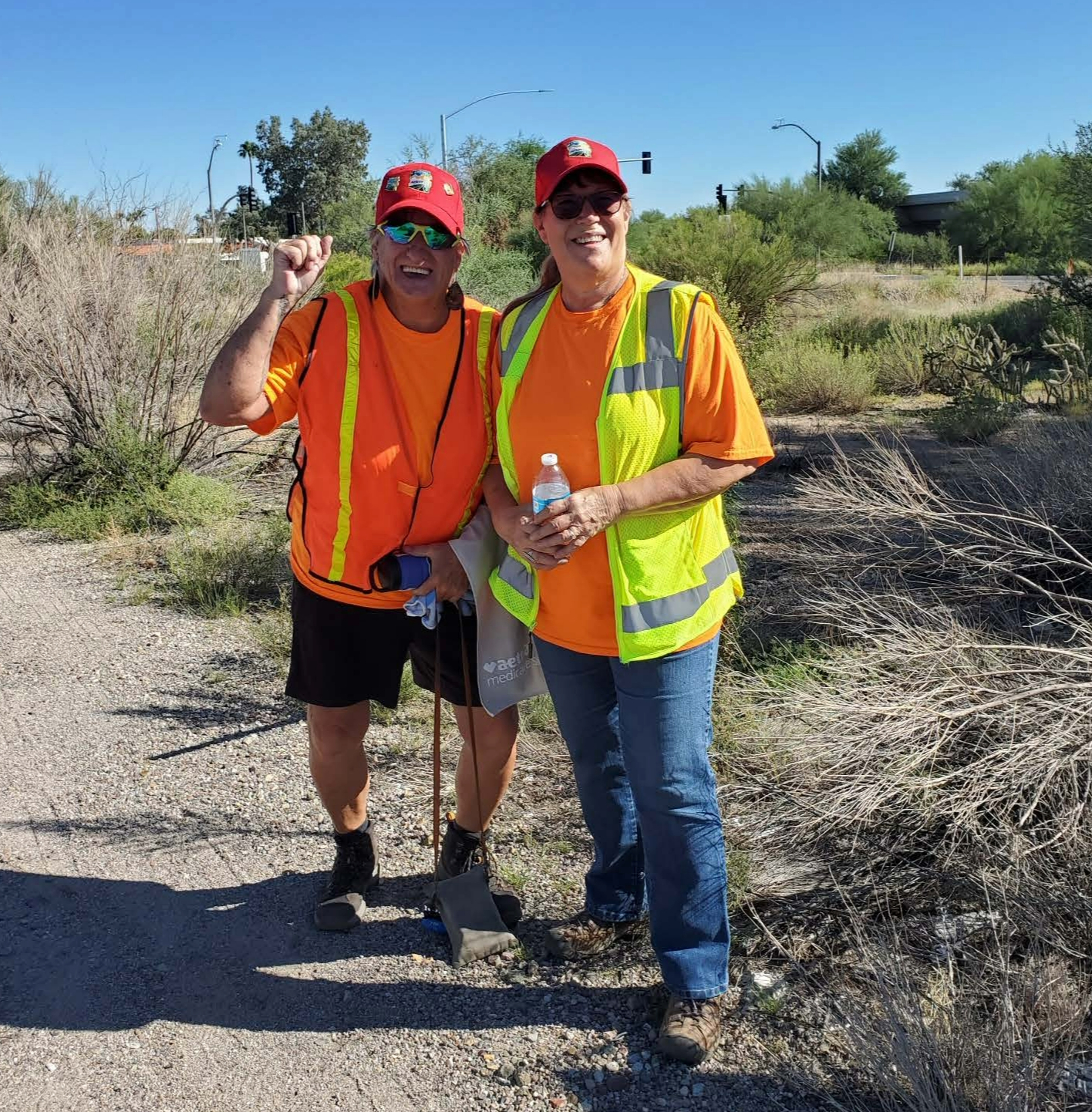 Two people pose for a photo during a litter clean-up event near a road.