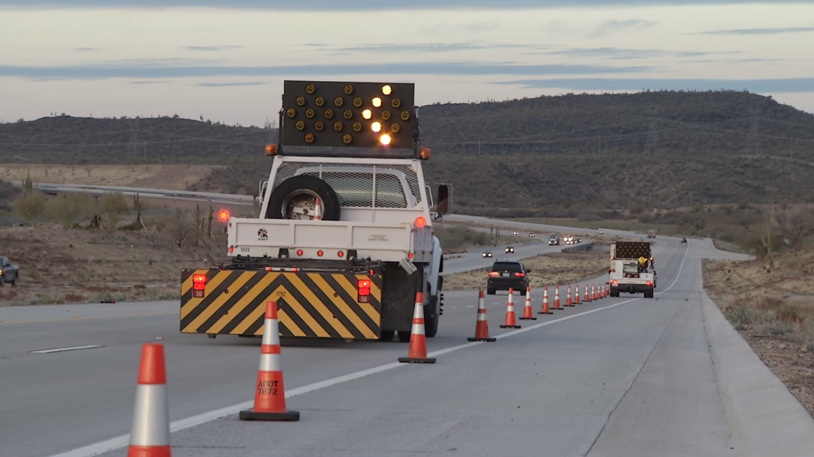 An ADOT cone truck is laying down traffic cones and followed by an attenuator truck in a worzone.