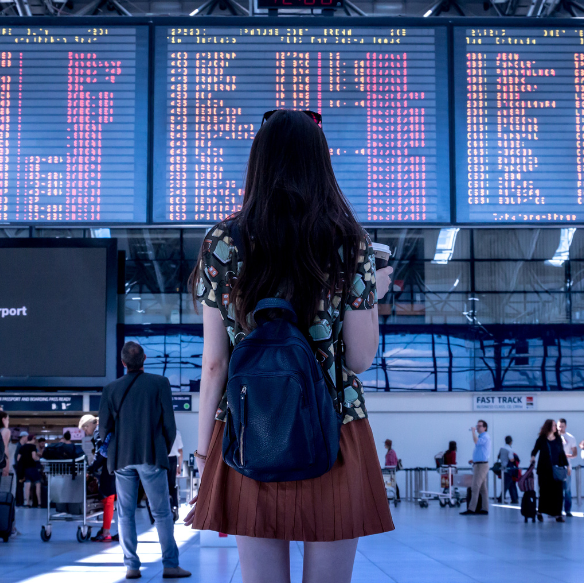 A woman stands in an airport, looking at a board the displays arrival and departure times.