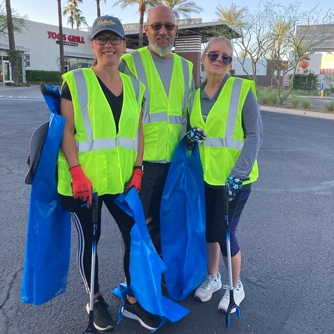 Three people in yellow safety vests pose for a picture in a parking lot.