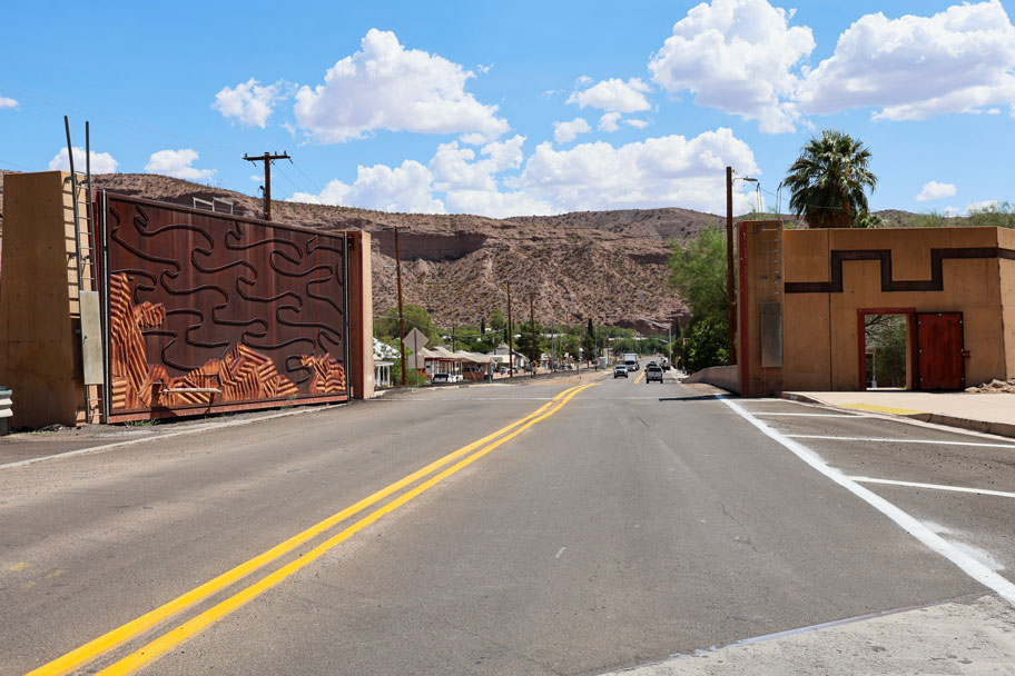Street view of US 191 in a small desert town, showing decorative gateway structures with artistic panels, road striping, and red rock hills in the background.