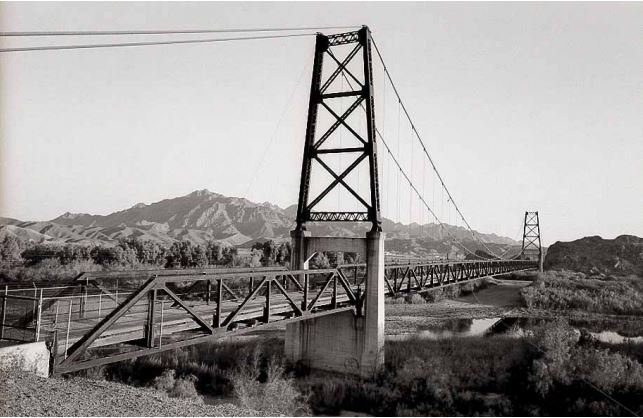 A black and white photo of a rural bridge over a river.