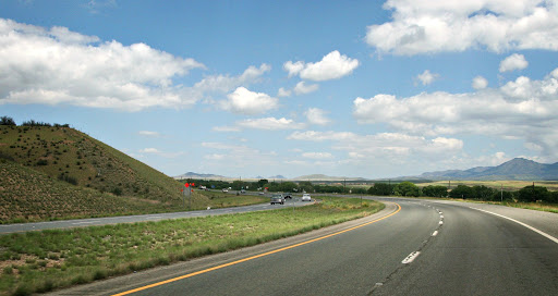 A curved highway with cars driving under a blue sky with scattered clouds and grassy hillsides.
