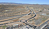 Aerial view of a highway interchange with multiple lanes, a roundabout, overpasses, and surrounding dry, open landscape.
