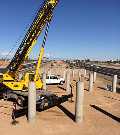 A yellow crane and concrete pillars at a highway construction site under a clear blue sky.