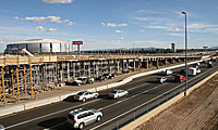 Cars driving on a highway next to an overpass under construction, with a stadium in the background.