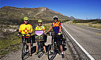 Three bike riders alongside freeway wearing helmets