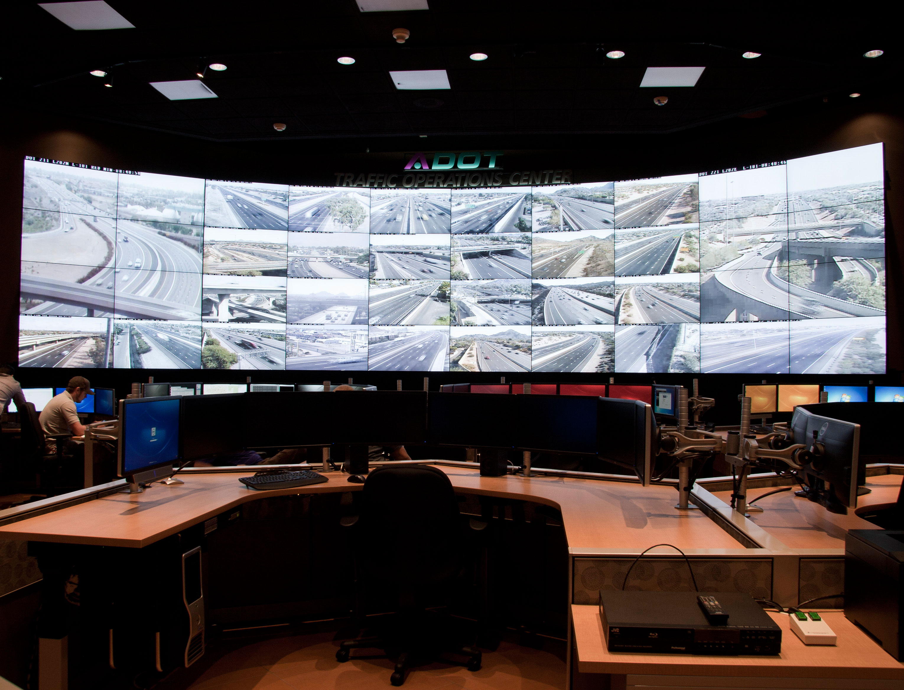 A traffic operations center with large screens displaying live highway camera feeds and empty workstations.