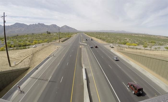 A wide highway in a desert landscape, with cars driving and mountains visible in the distance.