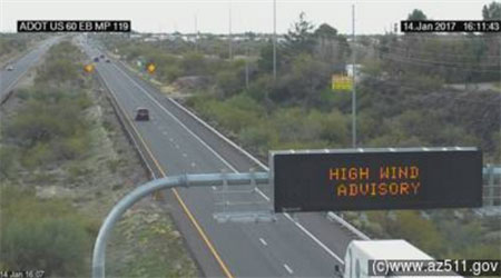 High wind advisory sign above a mostly empty highway with cars in the distance.