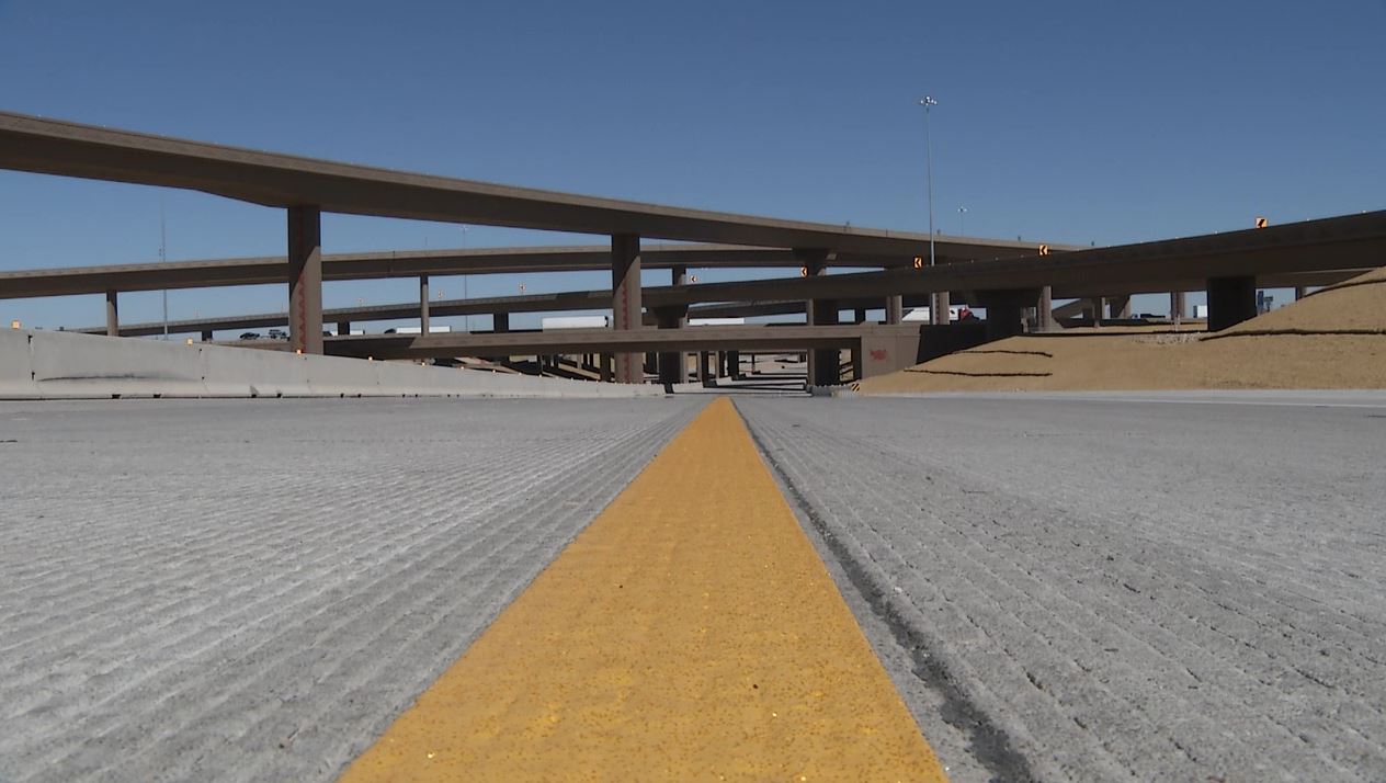 Low-angle view of a multi-level highway interchange with concrete overpasses under a clear blue sky, showing an empty road and a yellow center line.