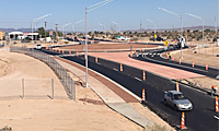 A newly paved multi-lane road with traffic cones and construction signage, surrounded by a dry, desert landscape under a clear sky.