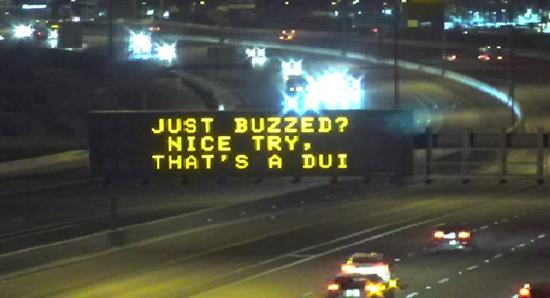 Highway sign at night reads: Just buzzed? Nice try, thats a DUI. Cars are visible on the road.