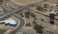 Aerial view of a highway overpass crossing above a railroad track with a train, surrounded by roads, buildings, and a water tower in a desert area.