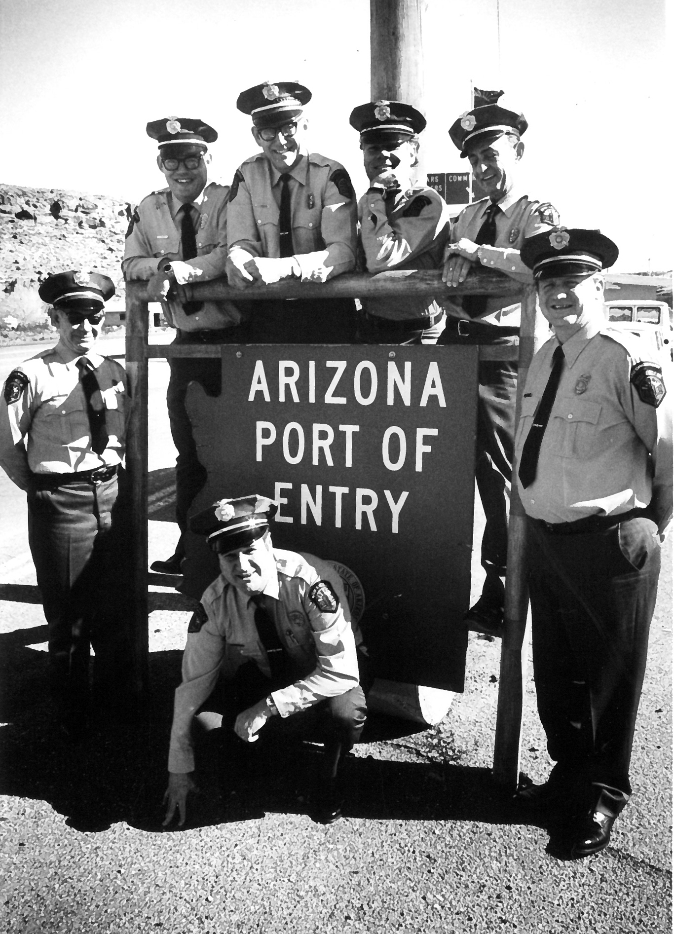 Black and white photo of seven MVD enforcement officers standing with Arizona port of entry sign