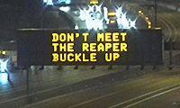 Highway electronic sign at night displays the message: DON’T MEET THE REAPER BUCKLE UP above lanes of traffic.