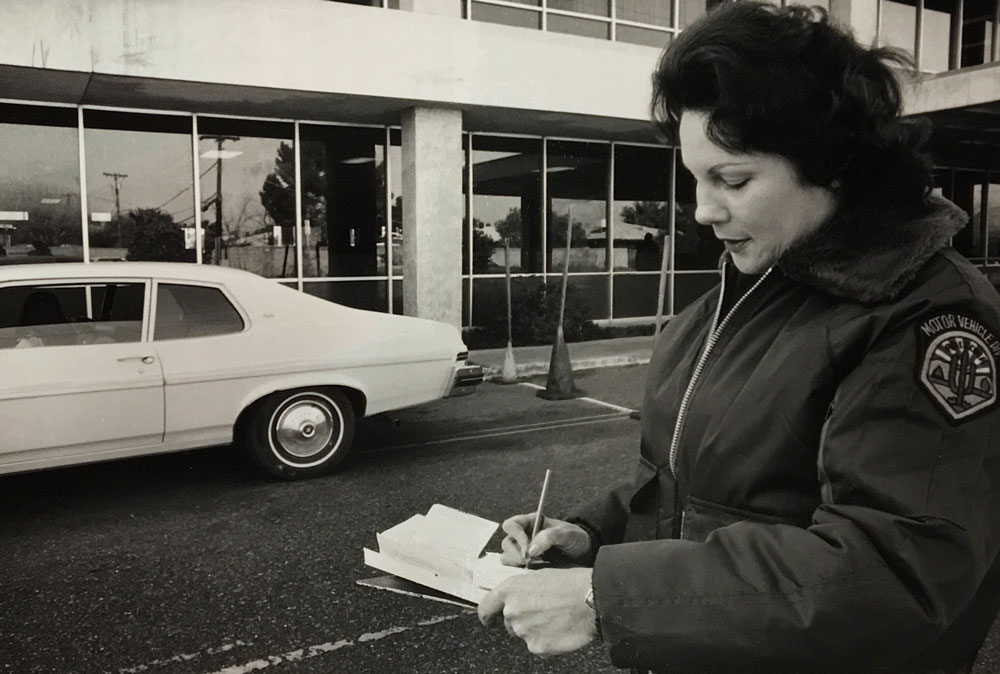 Black and white photo of road test reviewer writing on notepad in front of car