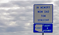 A roadside sign reads In Memory Mom Dad Tom Schlecht above a sign showing the outline of Arizona and text ADOT Adopt a Highway. Cloudy sky in the background.