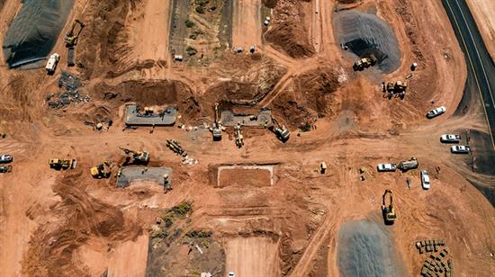 Aerial view of a large construction site with machinery, trucks, and dirt roads on reddish soil.