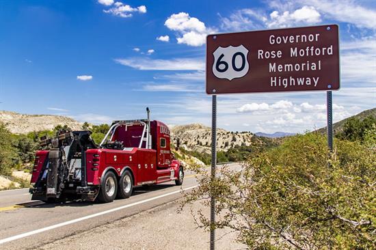 A red tow truck drives on a highway near a sign for Governor Rose Mofford Memorial Highway US 60.
