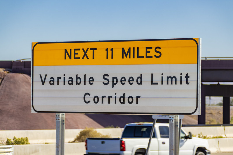 Road sign reads: Next 11 miles, Variable Speed Limit Corridor, with a white truck in the background.