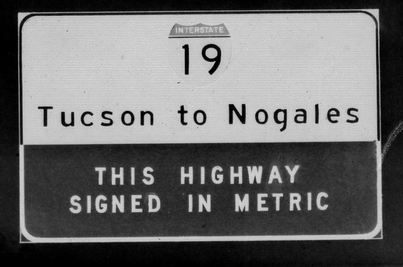Black and white road sign for Interstate 19, stating Tucson to Nogales and This highway signed in metric.