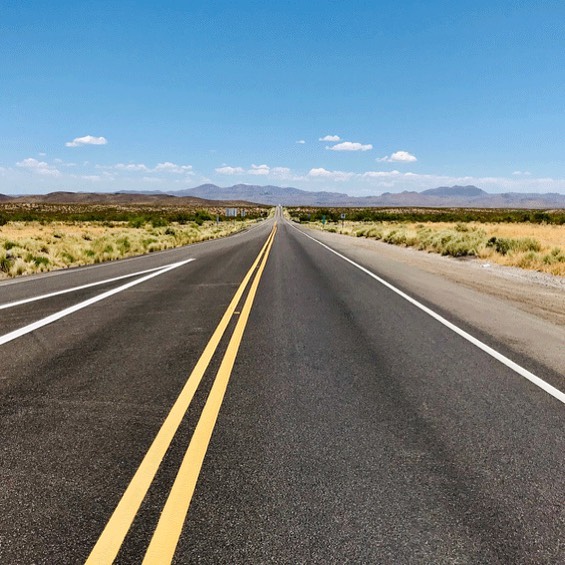A straight empty Northern Arizona highway stretches into the distance under a clear blue sky with mountains ahead.