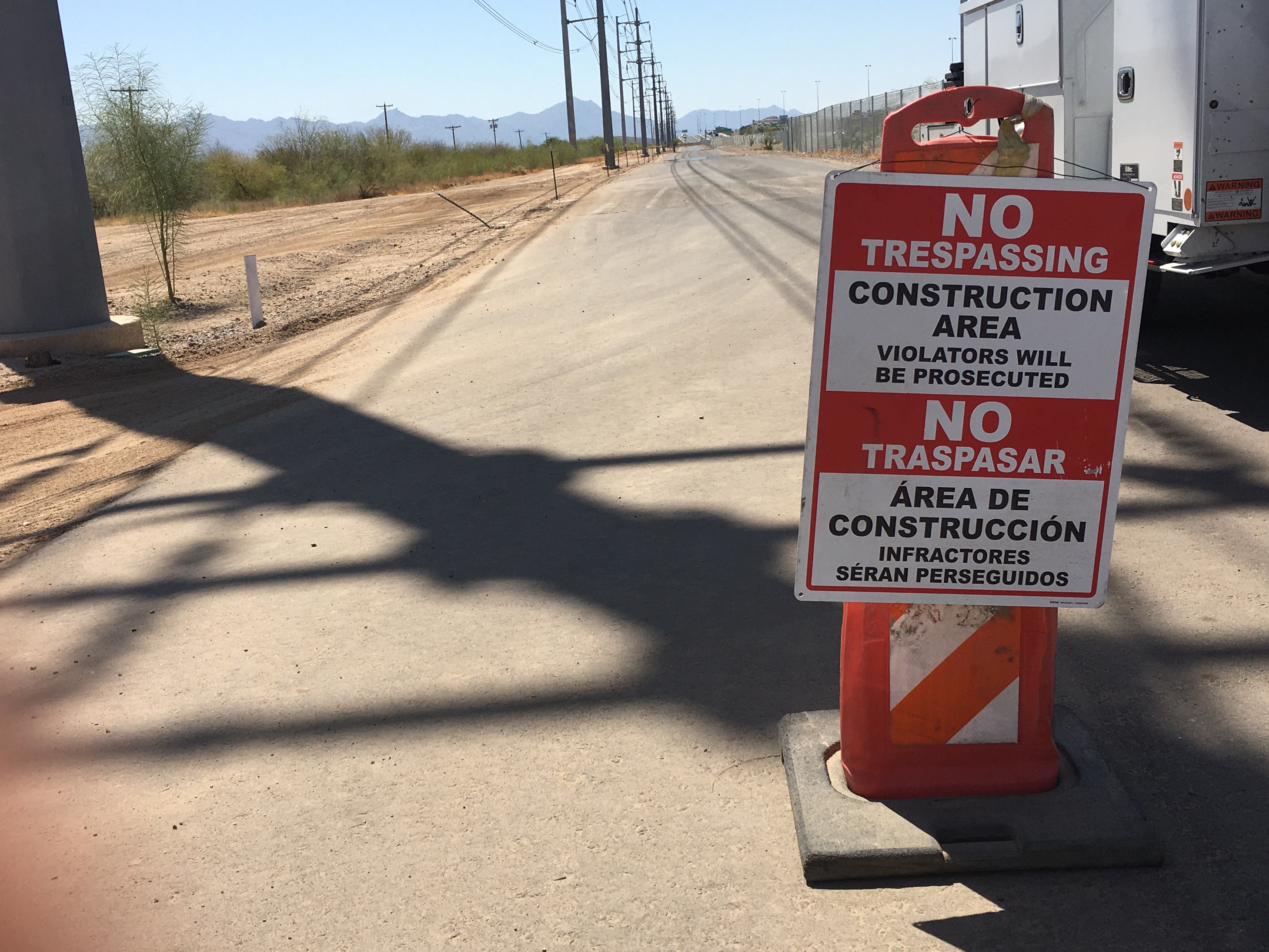 Orange barrier with a bilingual No Trespassing, Construction Area warning sign on a paved road.