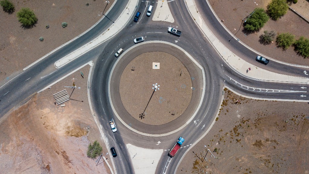 Aerial view of a roundabout with multiple cars driving, surrounded by desert landscape and sparse vegetation.