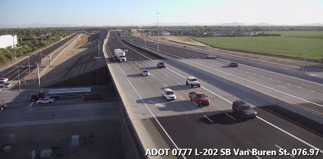 Several cars and trucks drive on a wide highway overpass near fields, under a clear sky.