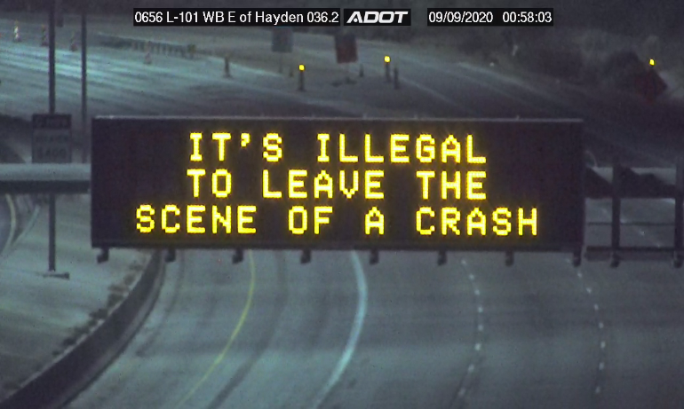 Electronic highway sign displays the message ITS ILLEGAL TO LEAVE THE SCENE OF A CRASH on an empty roadway at night.