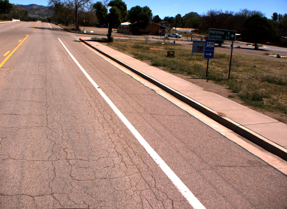 A road with a sidewalk and a sign showing directions to Harshaw and Lochiel under a clear sky.