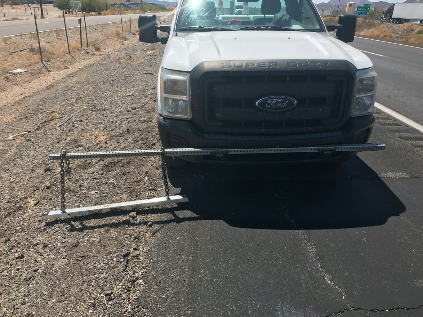 A white Ford Super Duty truck with a pickup bar mounted on its front bumper by the roadside.