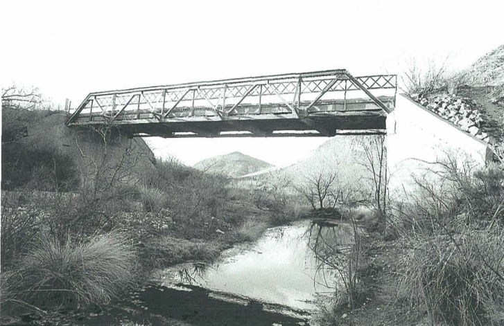 A metal truss bridge the Leslie Creek Bridge crosses over a small stream in a dry, grassy landscape with hills in the background.