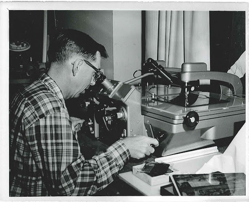 A man in glasses uses a large vintage photogrammetry reader at a desk.