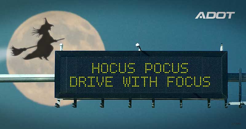 Highway sign reads HOCUS POCUS DRIVE WITH FOCUS with a silhouette of a witch on a broomstick flying in front of a full moon in the background. ADOT logo appears in the upper right corner.